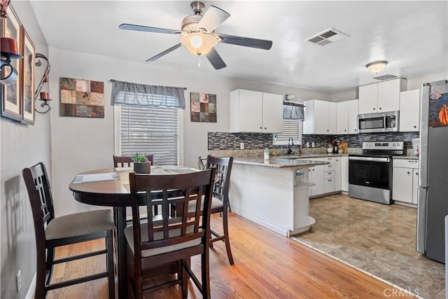 kitchen featuring white cabinets, light hardwood / wood-style floors, kitchen peninsula, and appliances with stainless steel finishes