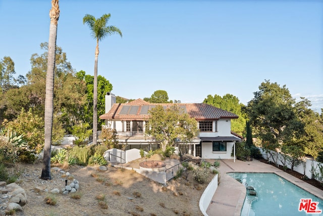 back of property with solar panels, a fenced in pool, and a patio