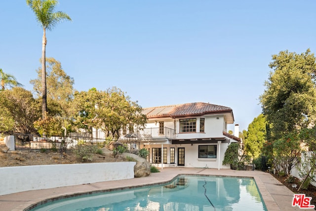 back of property with a balcony, a fenced in pool, a patio, and french doors