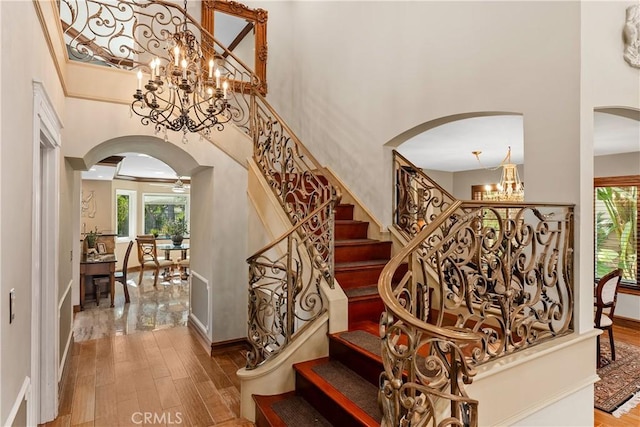 staircase featuring a chandelier, wood-type flooring, and a towering ceiling