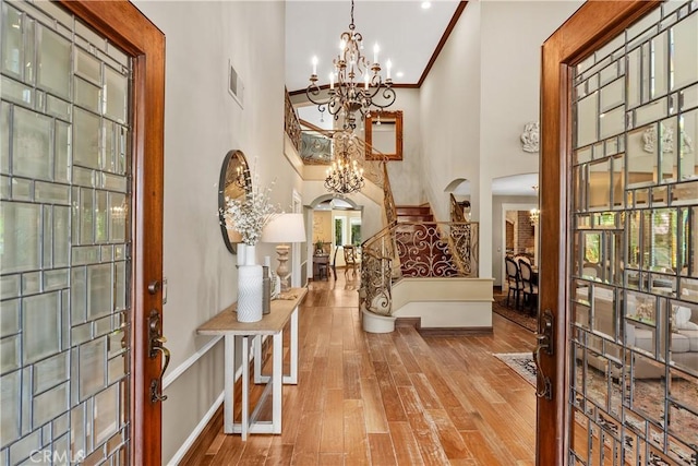 entryway with light wood-type flooring, ornamental molding, a high ceiling, and an inviting chandelier