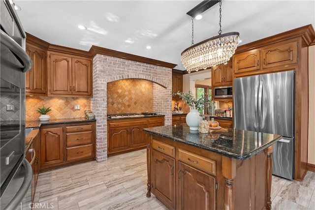 kitchen with appliances with stainless steel finishes, backsplash, decorative light fixtures, an inviting chandelier, and a center island