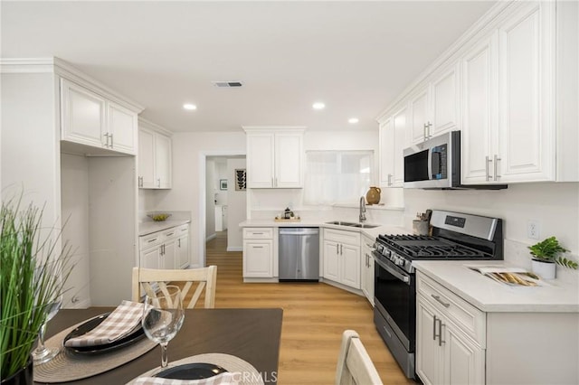 kitchen with white cabinets, stainless steel appliances, light hardwood / wood-style floors, and sink