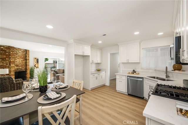 kitchen featuring sink, stainless steel appliances, a fireplace, white cabinets, and light wood-type flooring