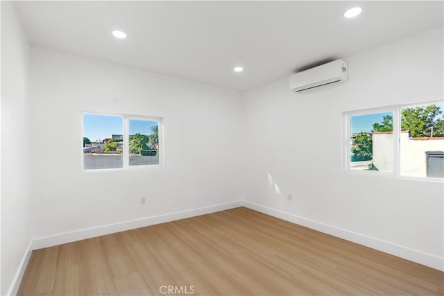 spare room with an AC wall unit, a wealth of natural light, and light wood-type flooring