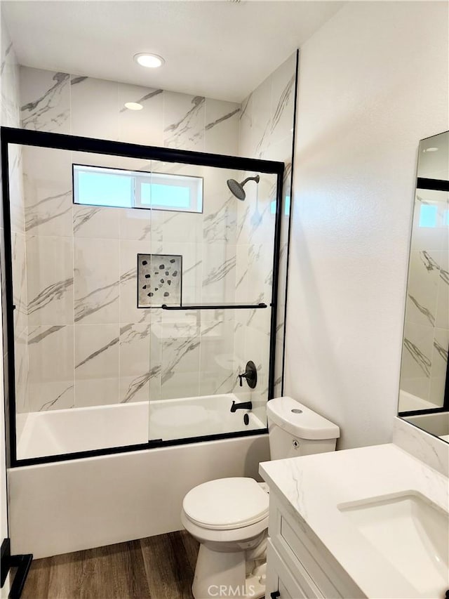 full bathroom featuring wood-type flooring, combined bath / shower with glass door, vanity, and toilet