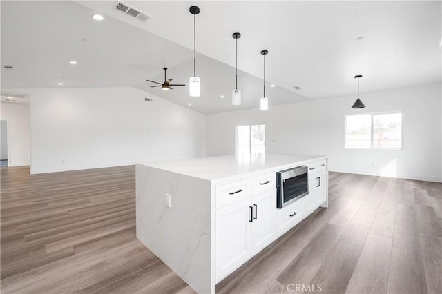 kitchen featuring light wood-style flooring, stainless steel microwave, visible vents, and a healthy amount of sunlight