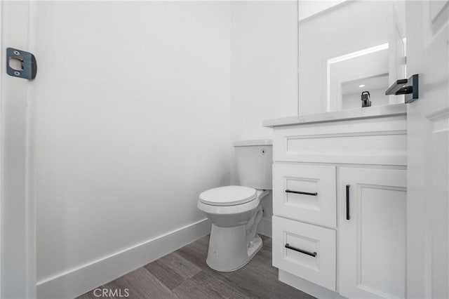 half bathroom with wood finished floors, vanity, toilet, and baseboards