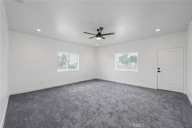 spare room featuring recessed lighting, a healthy amount of sunlight, dark carpet, and baseboards