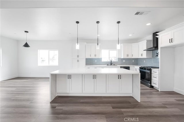 kitchen with light countertops, visible vents, white cabinets, stainless steel range with gas stovetop, and wall chimney exhaust hood