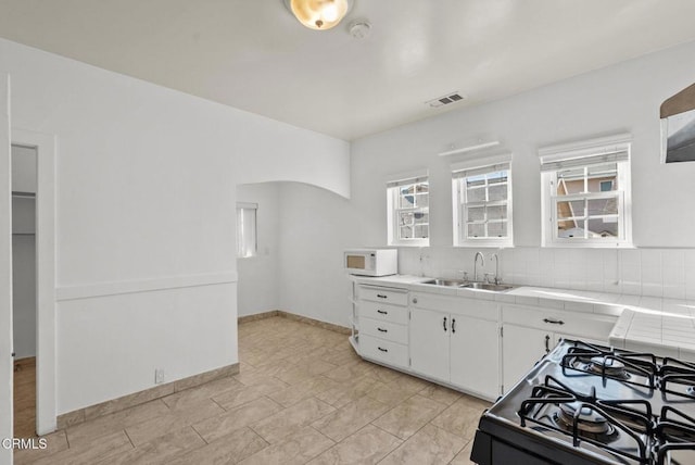 kitchen featuring black stove, tasteful backsplash, sink, white cabinets, and tile counters