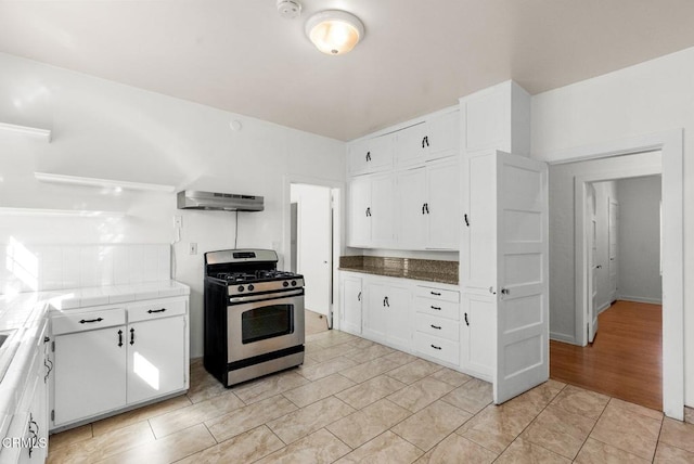 kitchen featuring stainless steel gas range oven, light hardwood / wood-style flooring, tile counters, white cabinetry, and extractor fan