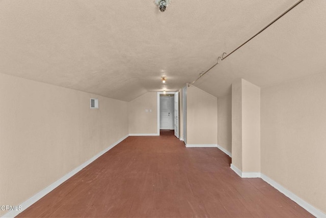 additional living space with a textured ceiling, wood-type flooring, and lofted ceiling