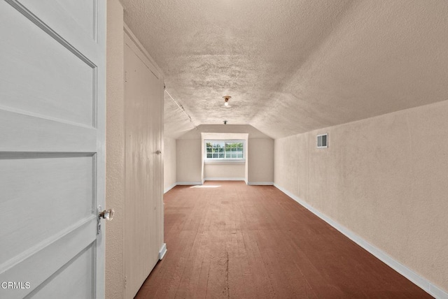 additional living space with a textured ceiling, hardwood / wood-style floors, and vaulted ceiling