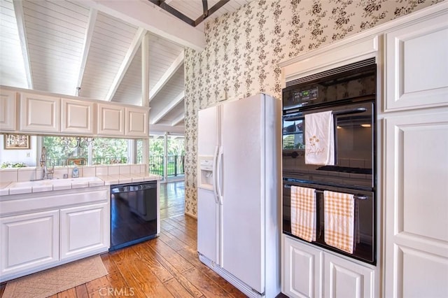 kitchen with sink, white cabinetry, tile countertops, light hardwood / wood-style floors, and black appliances