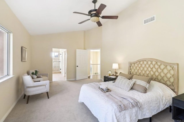 bedroom featuring ceiling fan, light colored carpet, high vaulted ceiling, and ensuite bath