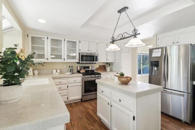 kitchen featuring appliances with stainless steel finishes, white cabinets, dark hardwood / wood-style floors, a kitchen island, and hanging light fixtures