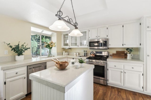 kitchen with appliances with stainless steel finishes, dark wood-type flooring, white cabinets, a center island, and hanging light fixtures