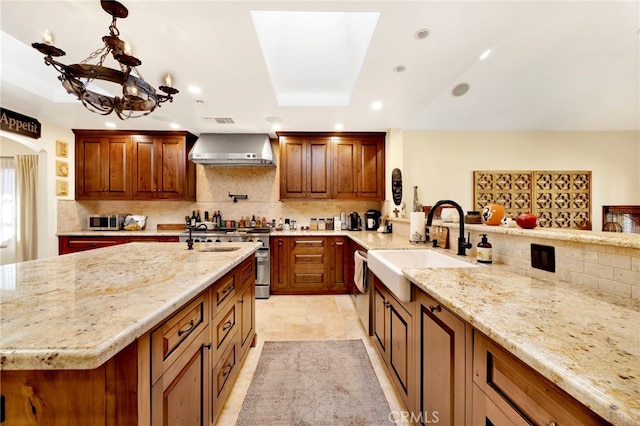 kitchen with pendant lighting, sink, wall chimney exhaust hood, light stone countertops, and a notable chandelier