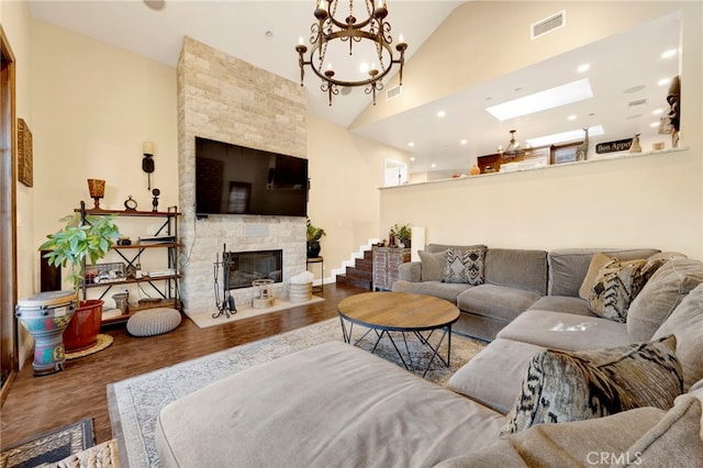 living room with hardwood / wood-style floors, high vaulted ceiling, an inviting chandelier, and a stone fireplace