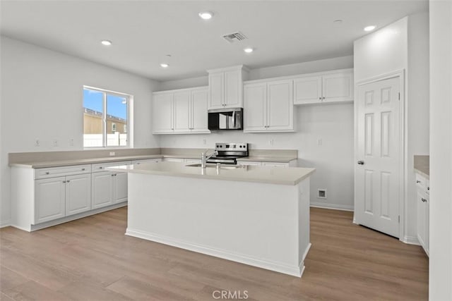 kitchen with stainless steel appliances, light hardwood / wood-style flooring, white cabinets, and an island with sink