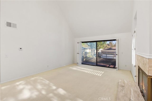 unfurnished living room featuring light carpet, high vaulted ceiling, and a tiled fireplace