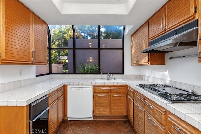 kitchen featuring dark parquet flooring, white dishwasher, stainless steel gas cooktop, sink, and tile counters