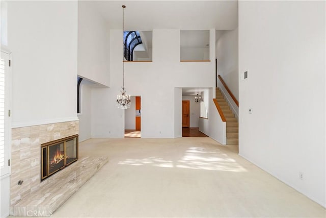 unfurnished living room featuring carpet, a tiled fireplace, a towering ceiling, and a notable chandelier