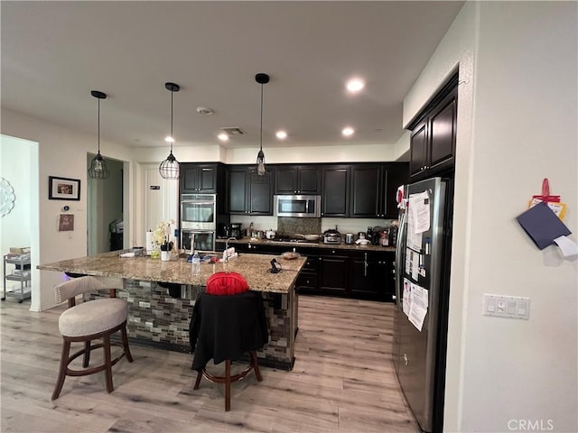 kitchen with pendant lighting, a breakfast bar area, light hardwood / wood-style flooring, an island with sink, and stainless steel appliances