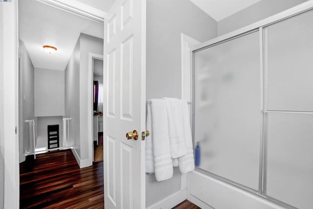 bathroom with wood-type flooring and bath / shower combo with glass door