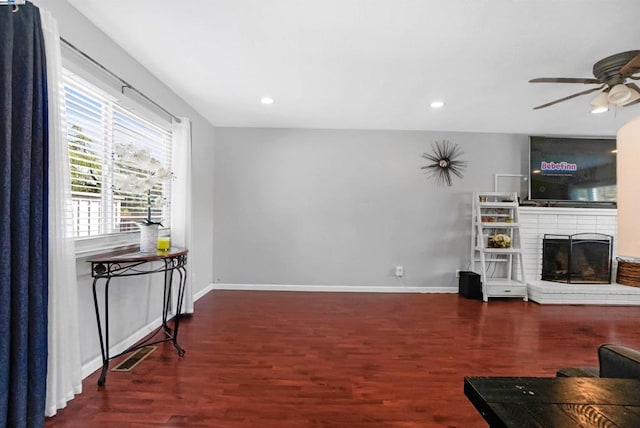 living room featuring ceiling fan, a fireplace, and dark wood-type flooring