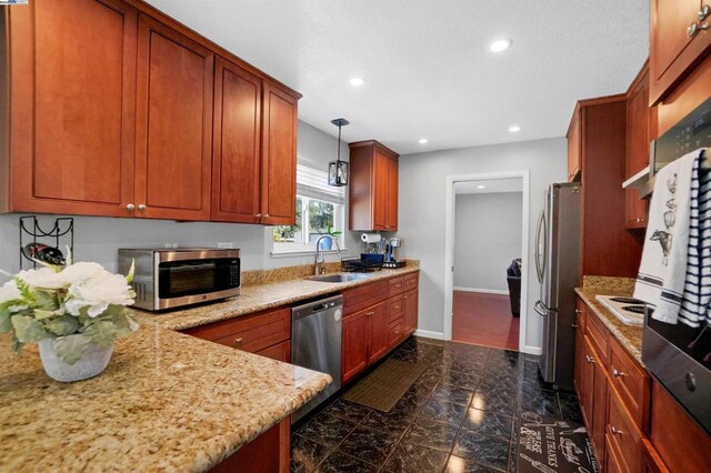 kitchen with pendant lighting, sink, light stone countertops, and stainless steel appliances