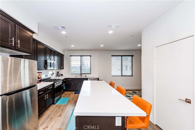 kitchen featuring dark brown cabinetry, light hardwood / wood-style flooring, a breakfast bar, a kitchen island, and appliances with stainless steel finishes