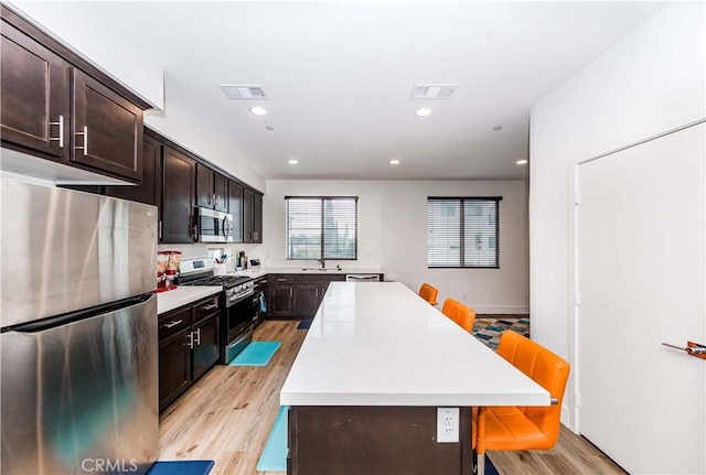 kitchen with a kitchen breakfast bar, light hardwood / wood-style flooring, a kitchen island, and appliances with stainless steel finishes