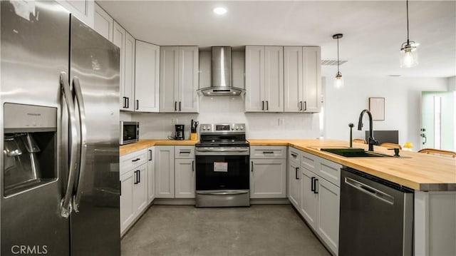 kitchen with sink, wall chimney exhaust hood, wood counters, decorative light fixtures, and appliances with stainless steel finishes