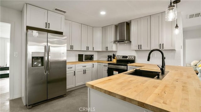 kitchen featuring wooden counters, sink, wall chimney exhaust hood, decorative light fixtures, and stainless steel appliances