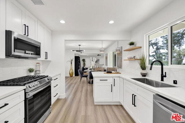 kitchen with white cabinetry, sink, stainless steel appliances, kitchen peninsula, and light hardwood / wood-style floors