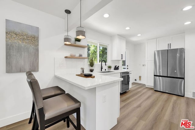 kitchen with white cabinetry, sink, hanging light fixtures, stainless steel appliances, and kitchen peninsula