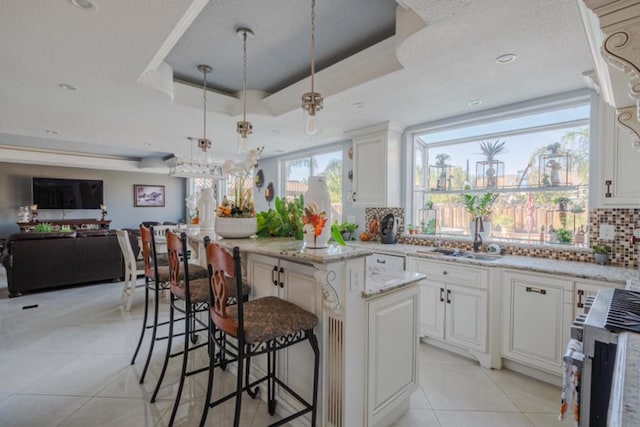 kitchen with sink, white cabinets, a center island, light tile patterned floors, and a raised ceiling