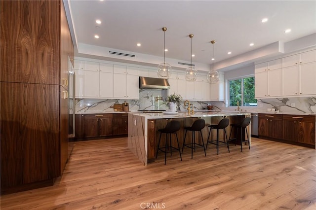 kitchen featuring tasteful backsplash, light countertops, a breakfast bar, under cabinet range hood, and a large island with sink