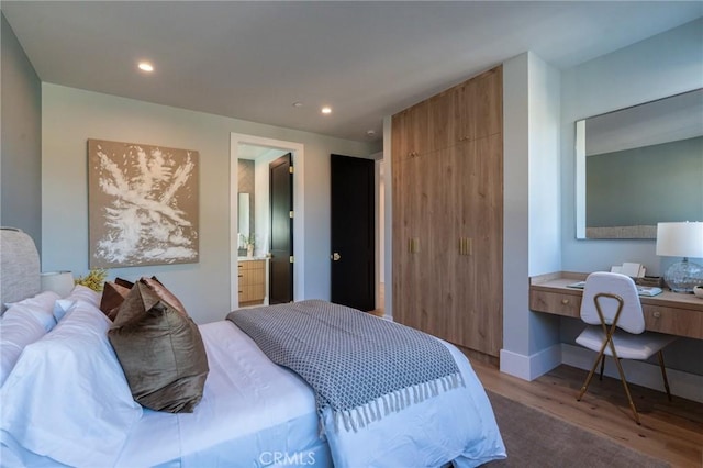 bedroom with hardwood / wood-style floors, built in desk, and ensuite bathroom