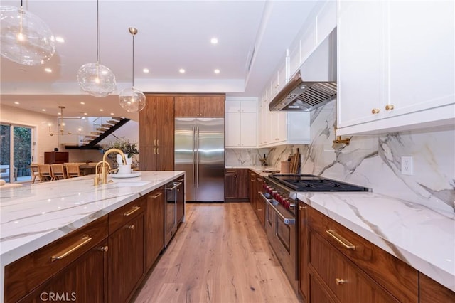 kitchen featuring white cabinetry, light hardwood / wood-style flooring, range hood, decorative light fixtures, and appliances with stainless steel finishes