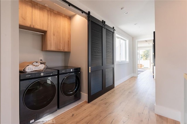 laundry area with cabinets, light wood-type flooring, washing machine and dryer, and a barn door