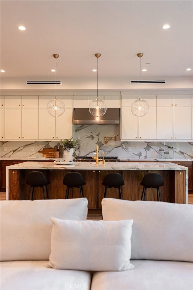 kitchen featuring a breakfast bar, backsplash, decorative light fixtures, and white cabinetry