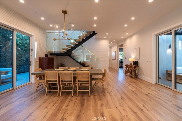 dining space featuring a wealth of natural light, stairway, an inviting chandelier, and wood finished floors
