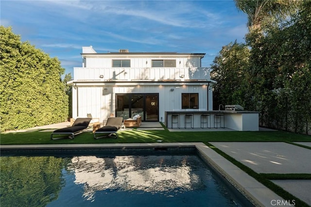 rear view of property featuring a patio area, area for grilling, outdoor dry bar, a balcony, and an outdoor pool