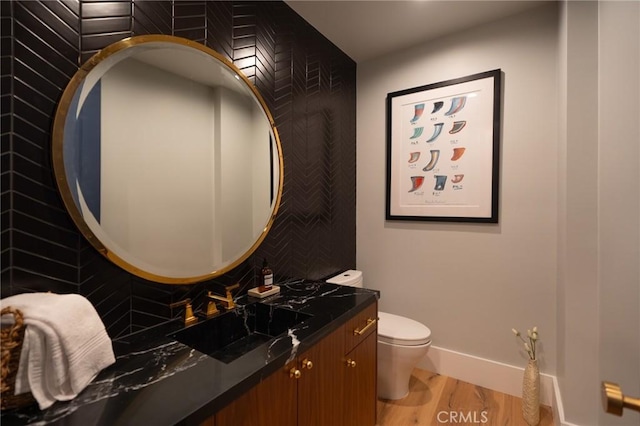 bathroom with tasteful backsplash, vanity, baseboards, toilet, and wood finished floors