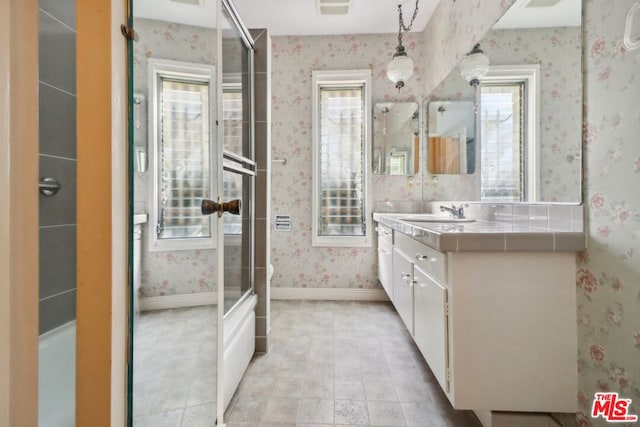 bathroom featuring plenty of natural light, bath / shower combo with glass door, and vanity