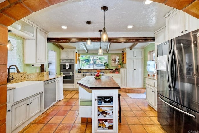 kitchen with stainless steel appliances, sink, beam ceiling, white cabinets, and a kitchen island