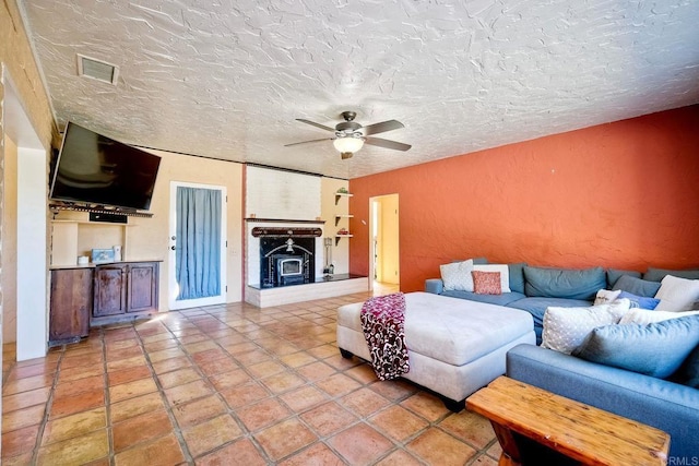 living room with tile patterned flooring, ceiling fan, a wood stove, and a textured ceiling